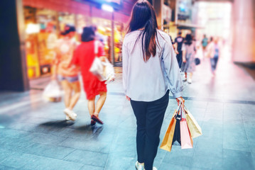 Woman holding shopping bag and walk alone in shopping street which have colorful light