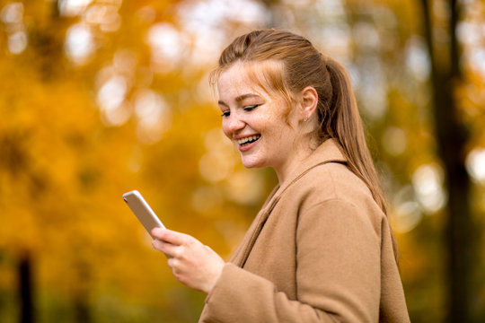 Image of young female using smartphone in the autumn park with colorful fallen leaves