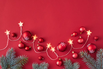 Flat lay frame with christmas garland, red christmas balls and spruce branches on a red background