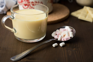 Zubereitung von heißer weiße Schokolade im Milchtopf mit Kakao Pulver und Marshmallows in Küche auf Holz Arbeitsfläche dunkel Hintergrund