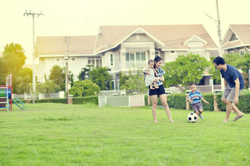 Portrait of Asian family playing football together in garden