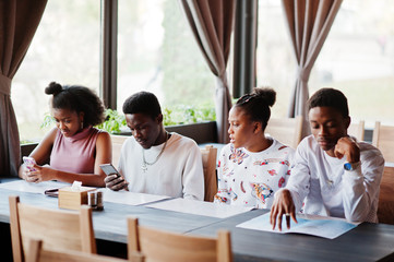 Happy african friends sitting and chatting in cafe. Group of black peoples meeting in restaurant and look at their mobile phone.