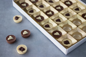 Round sweets made of white and milk chocolate with heart decor in a golden gift box. Close-up.