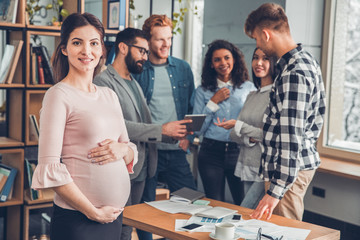 Startupers working together at office pregnant woman close-up looking camera happy while colleagues discussing project