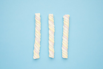 Colored long marshmallows on a blue background, delicious sweets flat lay