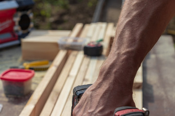 Photography of woodworking in industry. A worker makes a product from wooden blanks. The concept of street production of wooden blocks and plywood. Bright sunny weather in early autumn.