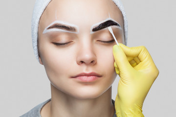 The make-up artist wipes the henna paint off the girl's eyebrows. The procedure of dyeing eyebrows...