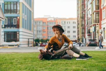 Stylish girl playing with a beautiful brown puppy on the lawn, smiling and stroking the dog. Beautiful lady is having fun on the grass with a dog in the yard on a background of a modern city block.