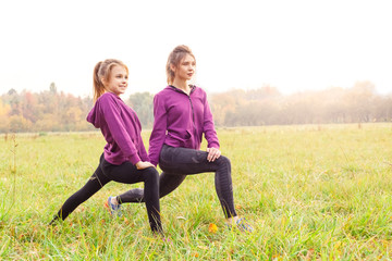 Outdoors leisure. Sisters doing lunge exercise in the autumn park looking forward cheerful