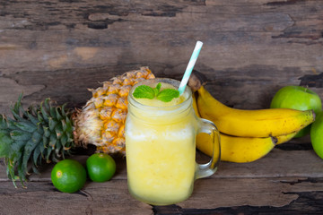 Banana with pineapple and apples, smoothies yellow fruit juice healthy drink delicious in a glass morning drink on a wooden background.