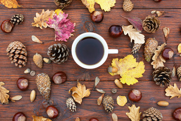 Cup of tea on a wooden table with autumn leaves, chestnuts and pine cones.