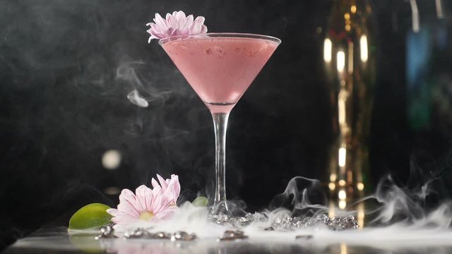 Wonderful pink non alcoholic cocktail shot with white dense smoke rising up. Shot in slow motion. Bright beverage placed on bar counter on black background. Hd
