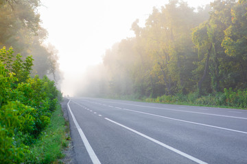 The asphalt road outside the city and thick fog above it in the morning