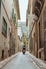 Man riding a motorcycle in an alley surrounded by old houses in the picturesque town of Soller, Mallorca, Spain. Vertical photo.