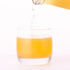Pouring a refreshing orange, yellow soda drink from bottle into glass on white background, close up