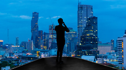 Fototapeta na wymiar Businessman standing using smart phone on open roof top balcony watching city night view.Business with ambition and vision concept.