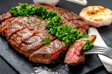 Ready to eat black Angus beef rib eye steak sliced with herbs, garlic and sauce on slate Board....