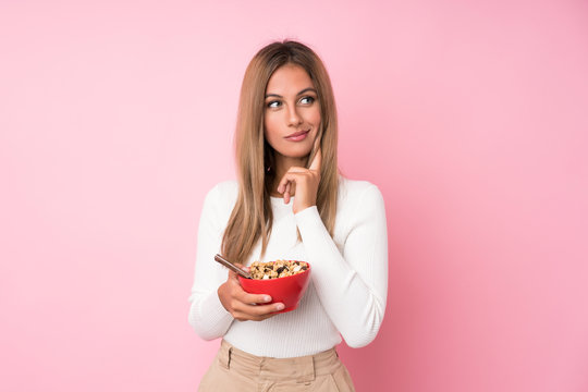 Young blonde woman over isolated pink background holding a bowl of cereals and thinking