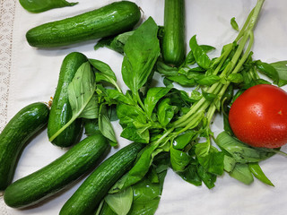 Fresh farming cucumbers, green basil and red ripe tomato. Vegetables and aromatic herbs covered with drops of water on the peel lie on the kitchen table. Selective focus