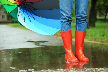 Woman with umbrella and rubber boots in puddle, closeup. Rainy weather