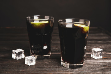 Refreshing soda drinks with ice cubes and lime on black wooden table
