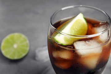 Glass of refreshing soda drink with lime on grey table, closeup. Space for text
