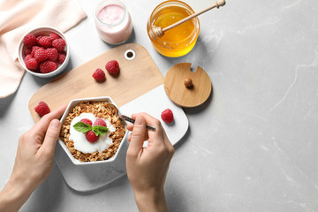 Woman eating delicious yogurt with granola and raspberries at grey table, top view. Space for text
