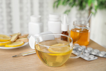 Glass cup of hot tea with lemon and different cold remedies on wooden table