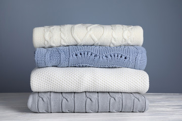 Stack of folded knitted sweaters on white wooden table against grey background