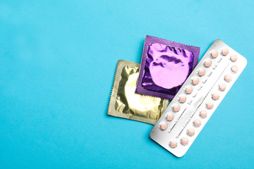 Condoms and birth control pills on light blue background, flat lay with space for text. Safe sex...