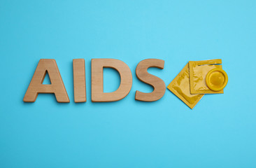 Yellow condoms and word AIDS made with wooden letters on light blue background, flat lay. Safe sex