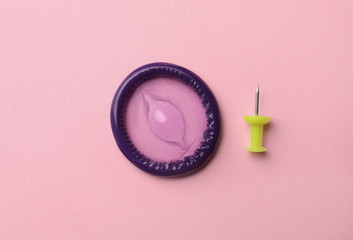 Purple condom and pin on pink background, flat lay
