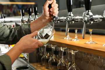 Bartender pouring fresh beer into glass in pub, closeup