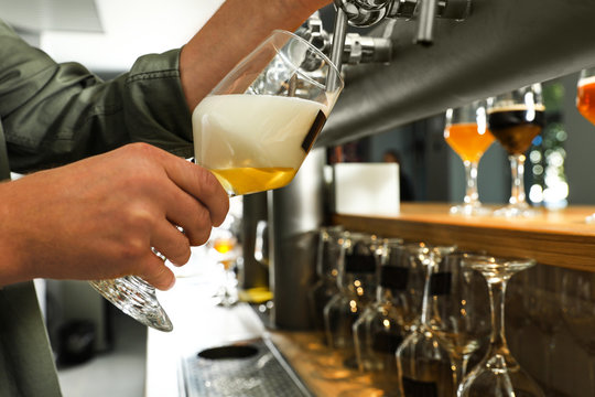 Bartender pouring fresh beer into glass in pub, closeup