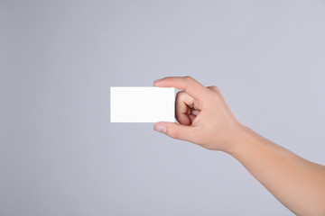 Man holding blank business card on grey background, closeup. Mock up for design