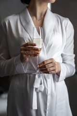 the bride in a white coat holds a glass of champagne in beautiful hands with an engagement ring.