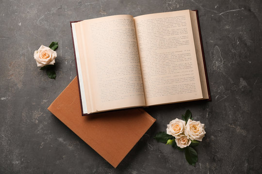 Open hardcover book and flowers on grey stone background, flat lay