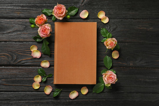 Flat lay composition with closed hardcover book and flowers on black wooden table