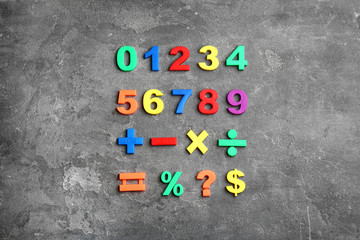 Colorful magnetic numbers and math symbols on grey stone background, flat lay