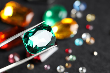 Tweezers with beautiful gemstone on blurred background, closeup. Space for text