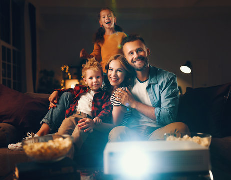 family mother father and children watching projector, TV, movies with popcorn in   evening   at home.