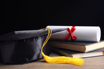 Graduation hat, books and student's diploma on wooden table