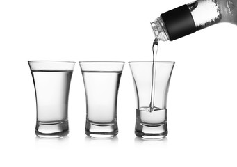 Pouring cold vodka into shot glass on white background