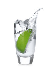 Lime slice falling into shot glass of vodka on white background