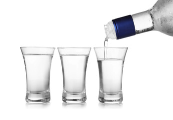 Pouring cold vodka into shot glass on white background