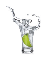 Lime slice falling into shot glass of vodka on white background