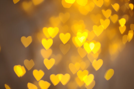Blurred view of gold heart shaped lights on light background