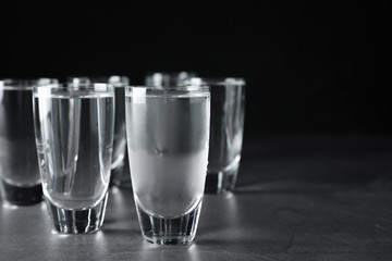 Shots of vodka on grey table against black background. Space for text