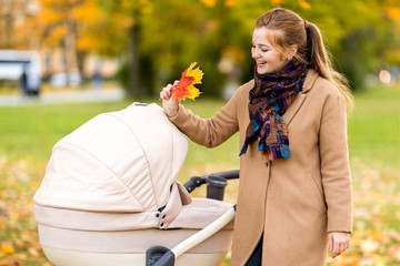 Young pretty mom smiling leaned over the stroller with the baby in the autumn park