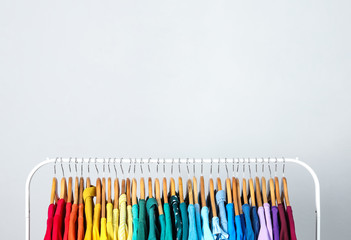 Rack with bright clothes on light blue background. Rainbow colors
